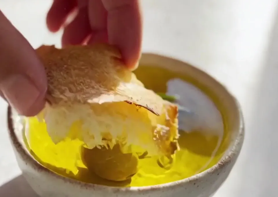 A hand dipping torn bread into a bowl of olive oil.